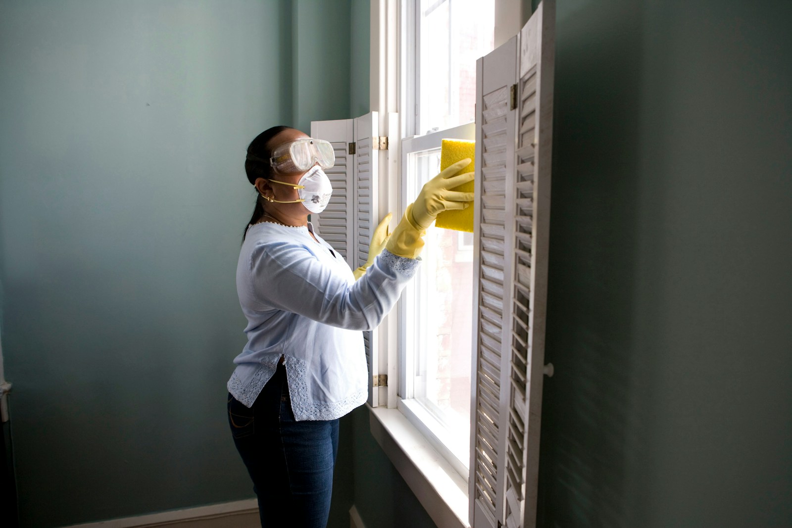 A homekeeper cleaning a window in a bright domestic room